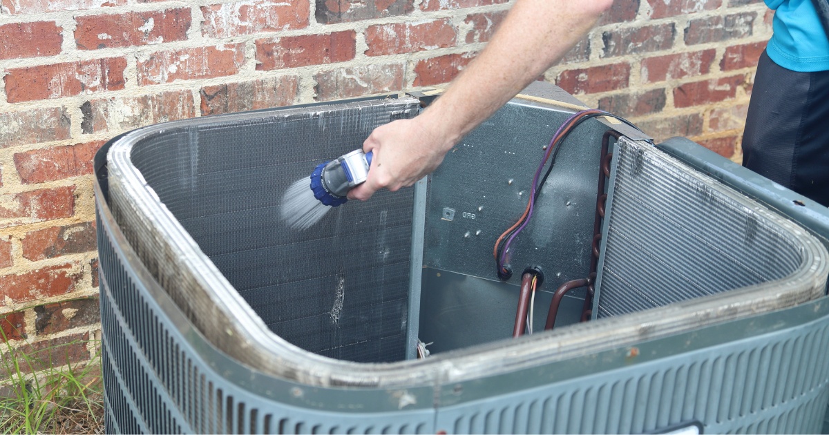 person using a water hose to clean the inside of an air conditioner condenser